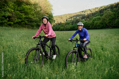 Happy active senior women friends cycling together outdoors in nature.