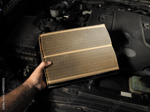 A mechanic holds a car air filter in his hand for auto maintenance in a repair shop, automotive part concept