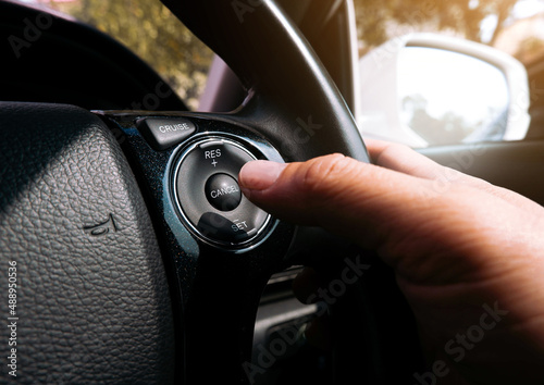 The driver presses the cruise control button on the car steering wheel with his hand