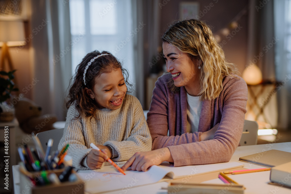 Little girl doing homework with her mother in evening at home.