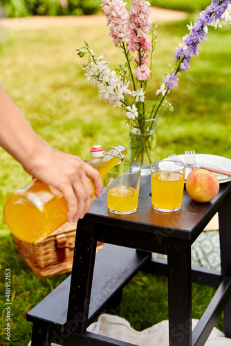leisure and drinks concept - close up of female hand pouring fruit juice from bottle to glass on picnic at summer park