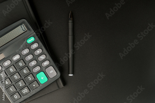 calculator notepad and pen on black background.