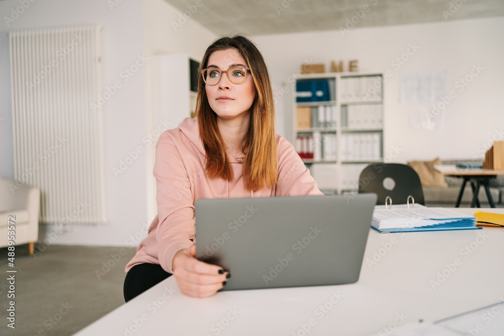 Thoughtful young businesswoman looking away sitting at table in home office Thoughtful young businesswoman looking away sitting at table in home office