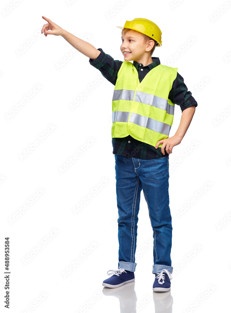 building, construction and profession concept - happy smiling little boy in protective helmet and safety vest pointing finger over white background