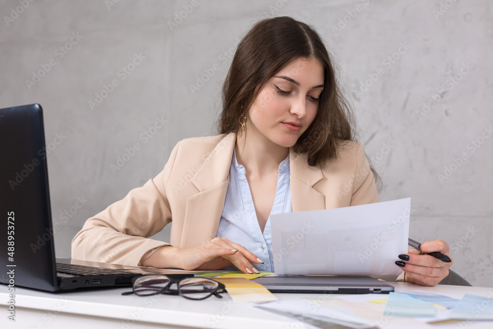 A young designer girl sitting at a table draws on a tablet. Makes business calculations on the computer. A young designer girl sitting at a table draws on a tablet. Makes business calculations on the computer.