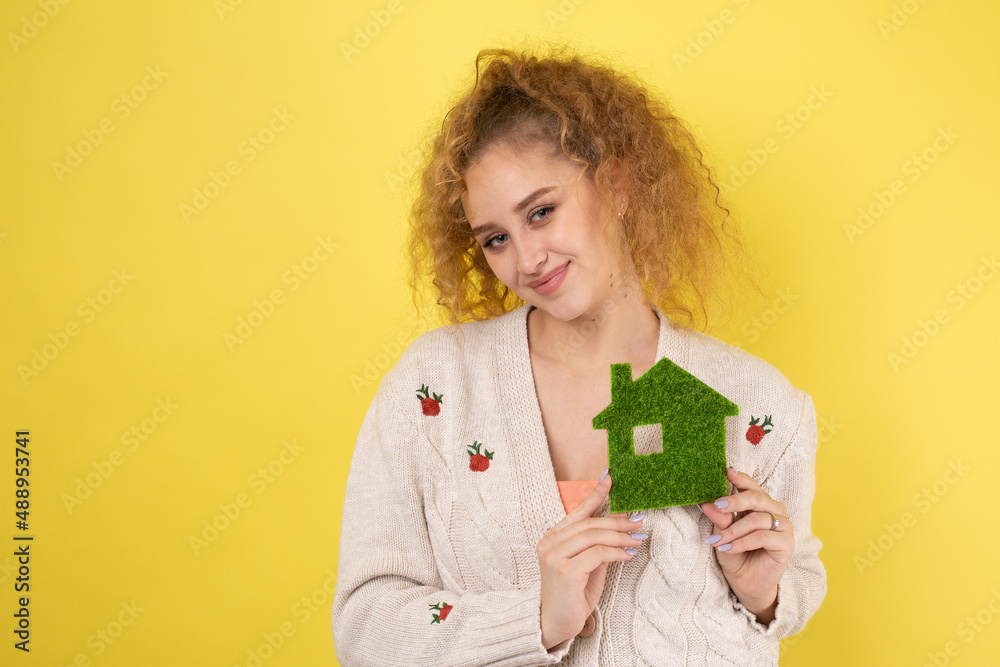 Happy house buyer. A young girl holds a model of a green house in her hands. The concept of green energy, ecology.