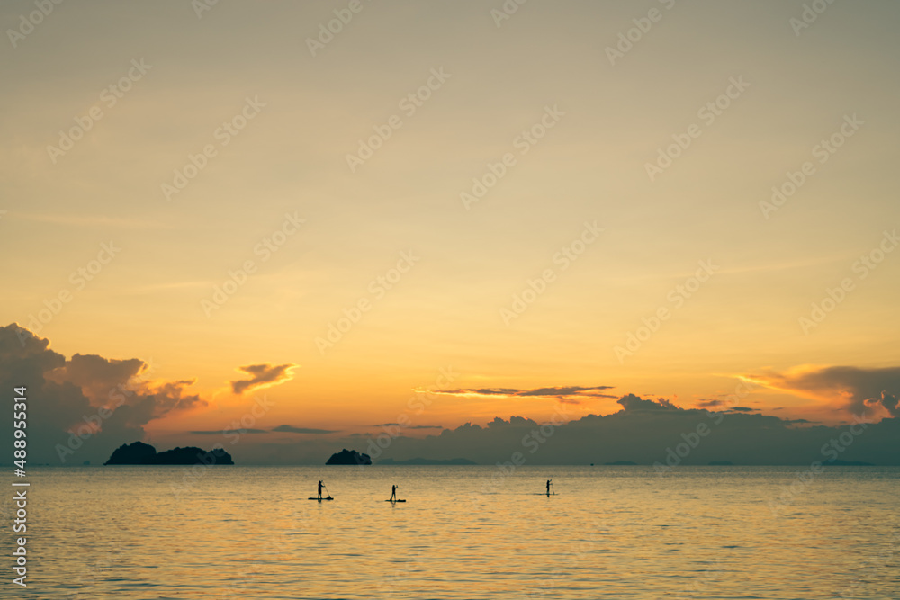People floats on stand up paddle boards against the backdrop of a spectacular colorful sunset over sea and islands on a summer evening. 