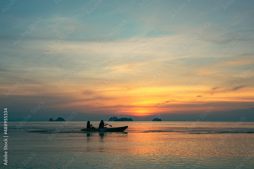 A couple is kayaking against the backdrop of a spectacular colorful sunset over sea and islands on a summer evening. 