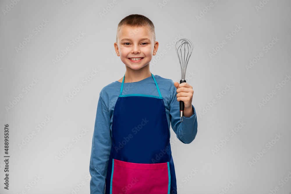 cooking, culinary and profession concept - happy smiling little boy in apron holding whisk over grey background cooking, culinary and profession concept - happy smiling little boy in apron holding whisk over grey background