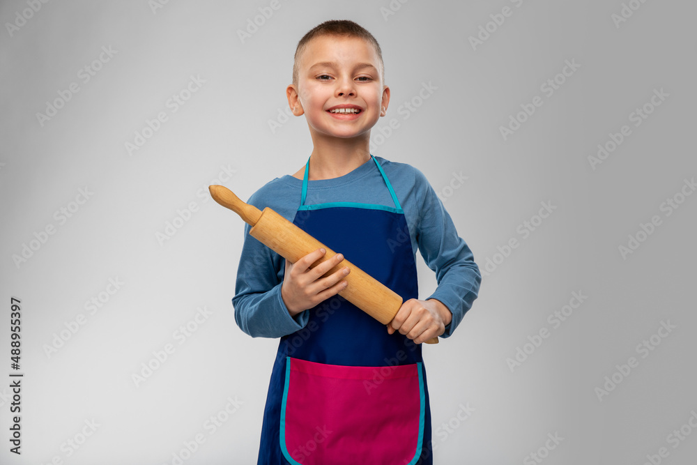 cooking, culinary and baking concept - happy smiling little boy in apron with rolling pin over grey background cooking, culinary and baking concept - happy smiling little boy in apron with rolling pin over grey background