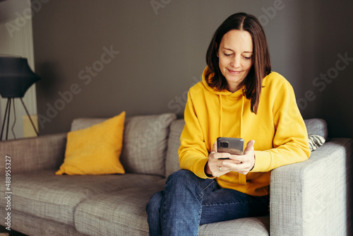 Woman wearing yellow hood sitting with smart phone on sofa at home