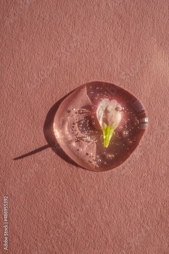 A drop of cosmetic gel with a flower on a pink background.