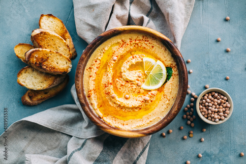 Fresh hummus in wooden plate with lemon and toasts, vegetarian food. Top view