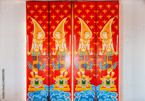 Vintage deity painting Thai design on ancient wooden doors. The door entrance of Buddhist temple at Wat Nong Waeng in Khon Kaen province, Thailand. photo