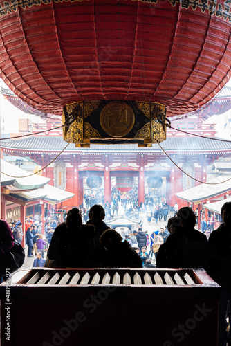 Silhouette of pilgrims praying in front of a saisen-bako or offertory box. The tourists are in Hondo, the main hall of Senso-ji Temple. photo