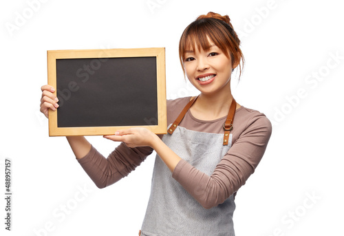 cooking, culinary and people concept - happy smiling female chef or waitress in apron with chalkboard over white background