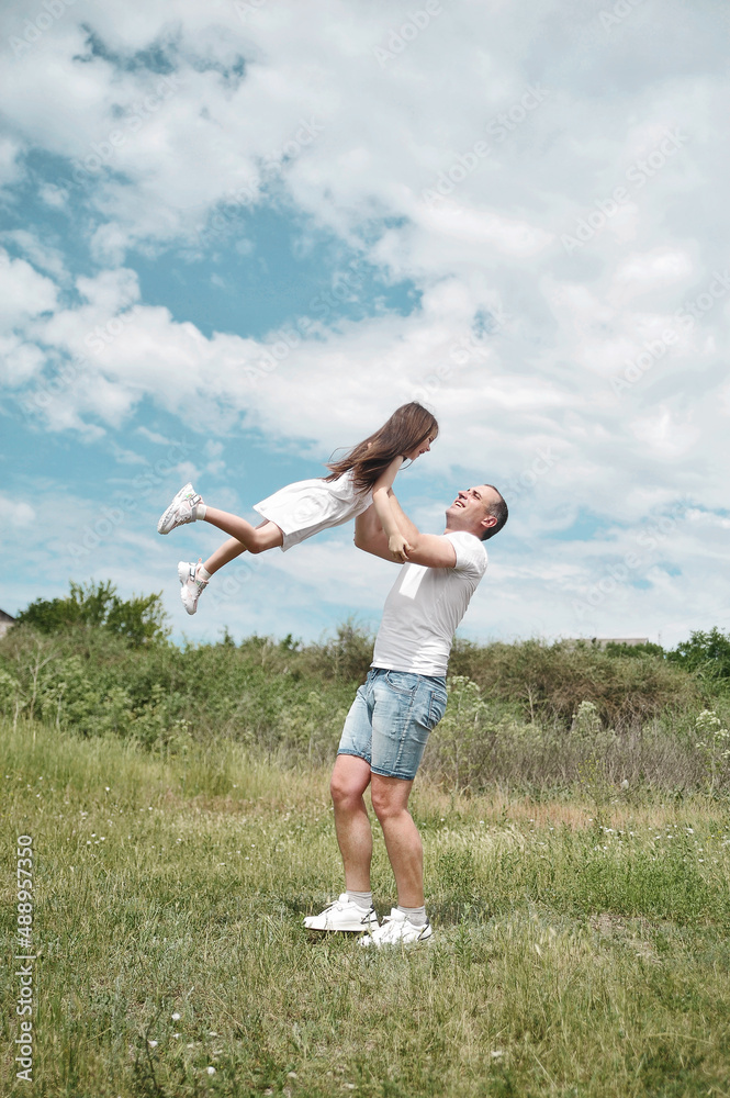 Fototapeta premium Dad and daughter have fun in the field . Happy family concept. Dad throws his daughter into the sky 