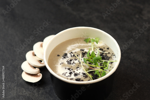 French cuisine hot food delivery - mushroom soup closeup in eco paper bowl  on black background. Delivery healthy eating concept.