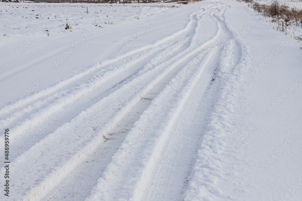 Snowy road in a field leading to pine forest. Winter road to nowhere in sunny day, snow-covered fresh car track. Car traces in a deep snow of remote rural area Snowy road in a field leading to pine forest. Winter road to nowhere in sunny day, snow-covered fresh car track. Car traces in a deep snow of remote rural area