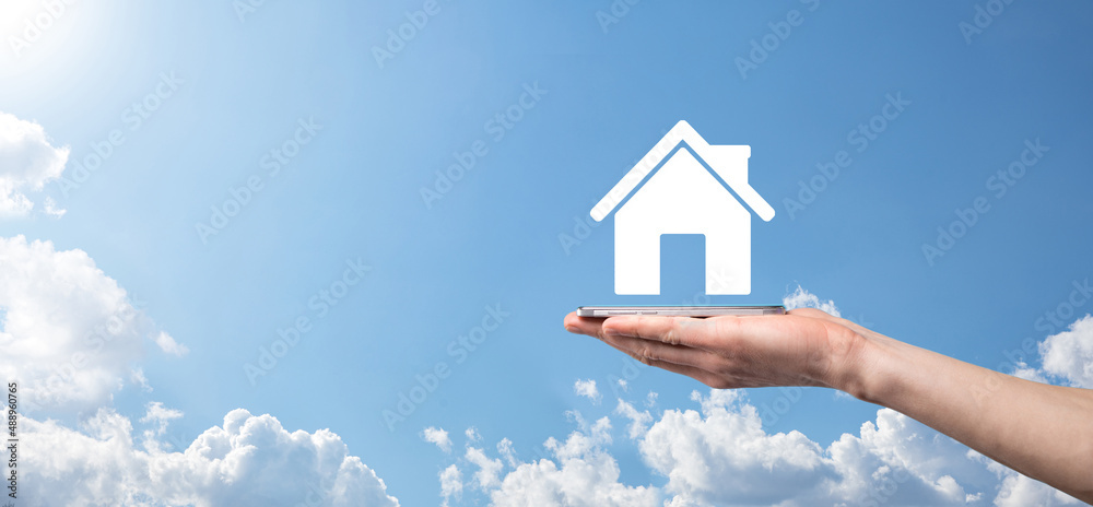 Naklejka premium Male hand holding house icon on blue background. Property insurance and security concept.Real estate concept.Banner with copy space.