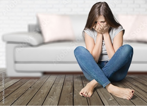 Depressed teen girl crying on the floor at home, suffering from bullying, being harassed online.