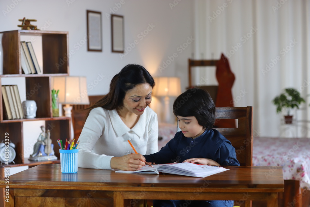 Young Indian mother teaching her school going son, Indian single mother, Parenting. Mother teaching her son at the study table, doing school homework, study time, vacation work Young Indian mother teaching her school going son, Indian single mother, Parenting. Mother teaching her son at the study table, doing school homework, study time, vacation work