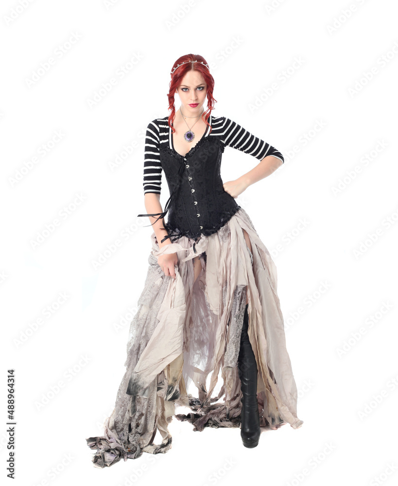 full length portrait of girl with red hair wearing black corset , torn gothic fantasy gown and leather boots. standing pose, isolated on white studio background. full length portrait of girl with red hair wearing black corset , torn gothic fantasy gown and leather boots. standing pose, isolated on white studio background.