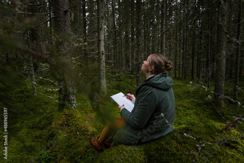 Woman sits in mossy green forest with sketch pad 