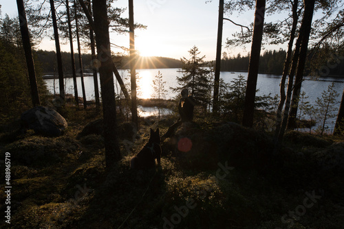Woman and dog enjoying sunrise in the forest by a lake