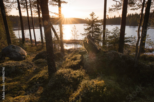 Woman and dog enjoying sunrise in the forest by a lake