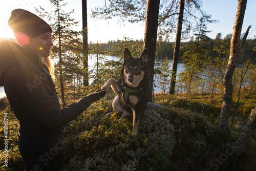 Woman and dog shaking hands in the forest by a lake