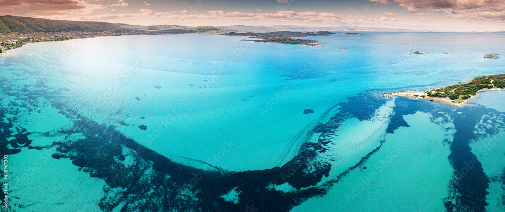 Aerial view of the paradise seashore with various shades of turquoise water. Coral reefs and secluded sandy beaches near the resort village of Vourvourou in Sithonia, Halkidiki.