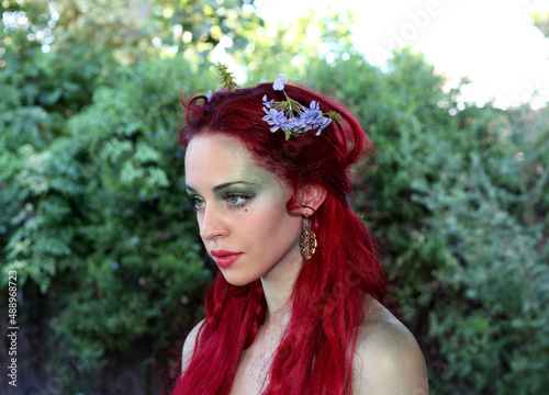 fantasy portrait of fairy girl with flowers in red hair and a pretty green dress, posing in enchanted forrest background.