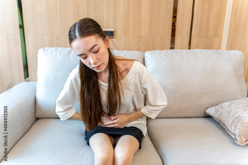 Caucasian woman sitting on the sofa couch having stomachache due to period or menstruation symptom Caucasian woman sitting on the sofa couch having stomachache due to period or menstruation symptom