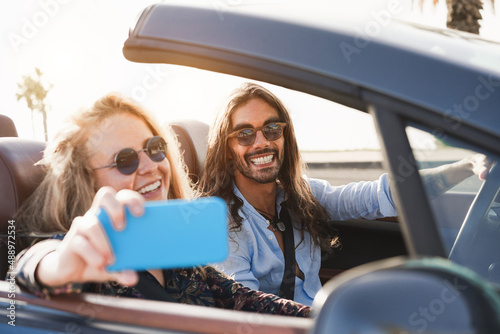 Young couple having fun doing selfie inside convertible car during summer vacation - Travel concept - Focus on man face © DisobeyArt