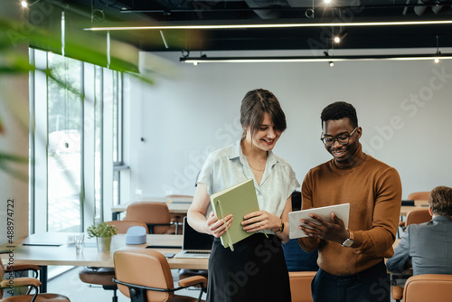 Happy Businesswoman and Businessman Using Digital Tablet Together at Work. 

Two smiling colleagues analyzing business report on a tablet while unrecognizable multi-ethnic team working at desk.