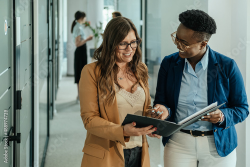 Two Happy Female Colleagues Holding Files with Business Report and Reading it Together at Work