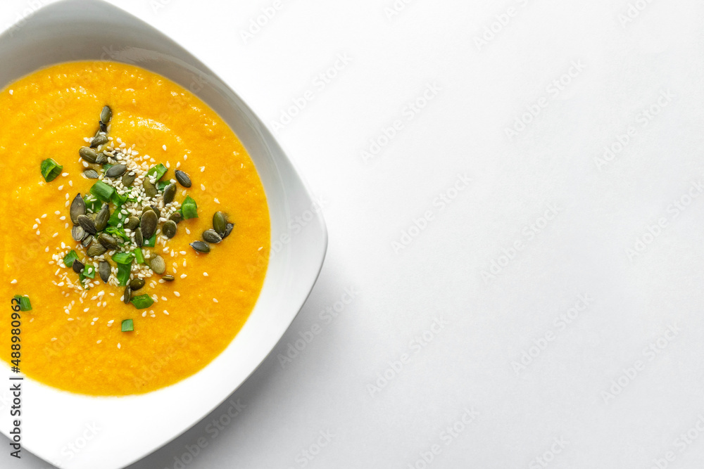 Pumpkin cream soup with green onion and pumpkin sesame seeds in white soup plate. Isolated on white background. Copy space. Vegetarian vegetable healthy food. Pumpkin cream soup with green onion and pumpkin sesame seeds in white soup plate. Isolated on white background. Copy space. Vegetarian vegetable healthy food.