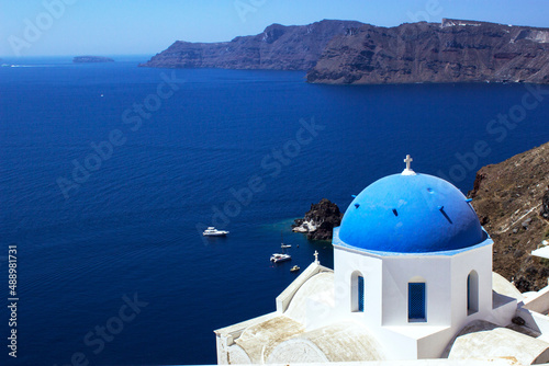 Church of Santorini with its traditional blue dome with the sea and cliffs in the background and boats anchored in a small harbor  travel concept.