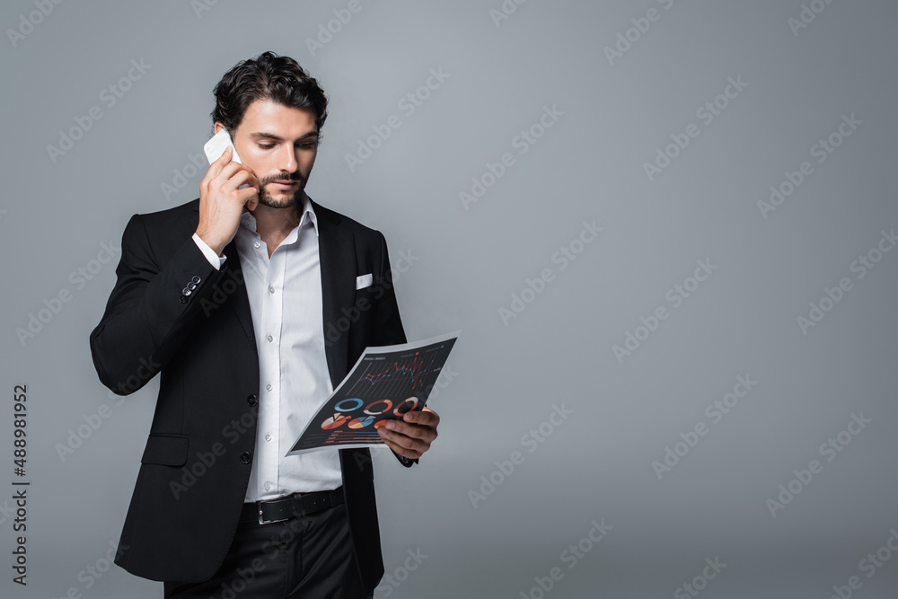 businessman in formal wear looking at charts and talking on mobile phone isolated on grey businessman in formal wear looking at charts and talking on mobile phone isolated on grey