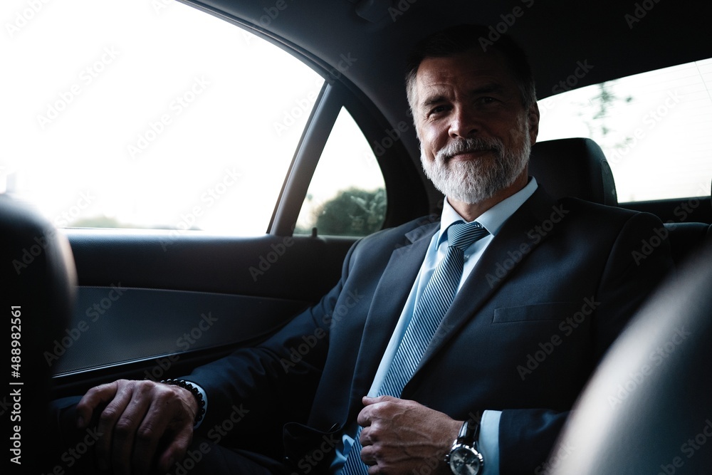 Mature handsome businessman is sitting in luxury car. Serious bearded man in suit.