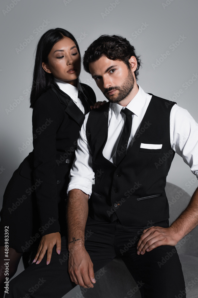 elegant asian woman near man in formal wear sitting on grey background elegant asian woman near man in formal wear sitting on grey background