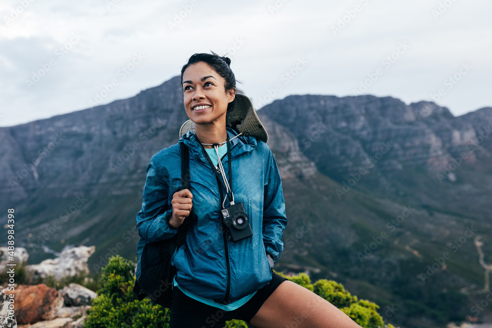 Portrait of a smiling woman relaxing during a mountain hike. Female with analog camera and backpack enjoying the view while standing on the top of the mountain. Portrait of a smiling woman relaxing during a mountain hike. Female with analog camera and backpack enjoying the view while standing on the top of the mountain.