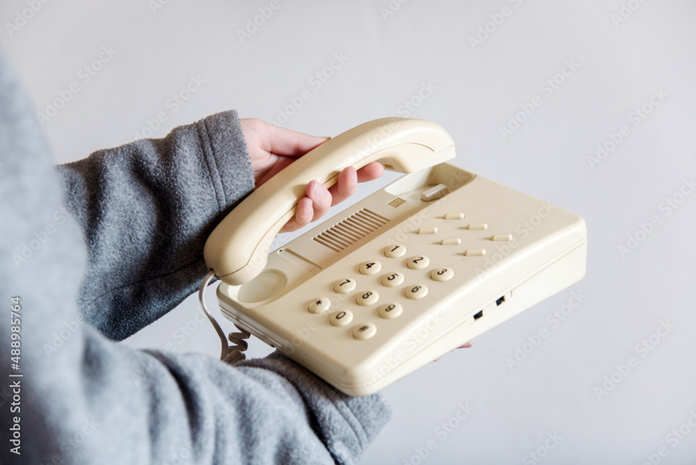Detalle de una mano de mujer descolgando un teléfono blanco
