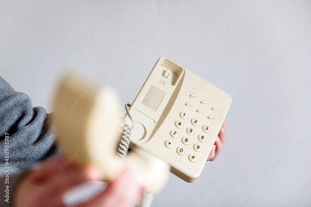 Detalle de una mano de mujer descolgando un teléfono blanco antiguo con cable. Mano sosteniendo el auricular de un teléfono fijo de casa u oficina. Concepto de atender una llamada telefónica. Detalle de una mano de mujer descolgando un teléfono blanco antiguo con cable. Mano sosteniendo el auricular de un teléfono fijo de casa u oficina. Concepto de atender una llamada telefónica.