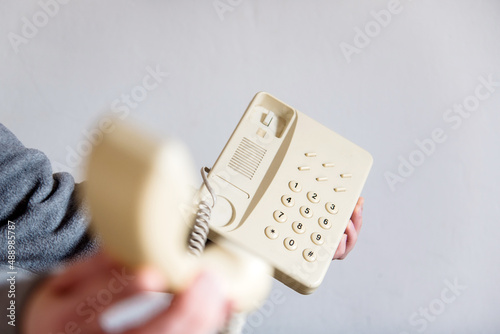 Detalle de una mano de mujer descolgando un teléfono blanco antiguo con cable. Mano sosteniendo el auricular de un teléfono fijo de casa u oficina. Concepto de atender una llamada telefónica. photo