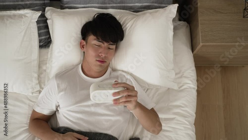high angle view of an overslept asian male woken by alarm calling and getting out of bed in shock because he is late for work in the morning at home.