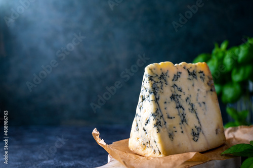 Blue cheese, dor blue or roquefort mold cheese slice on cutting board with basil leaves, lifestyle food. photo