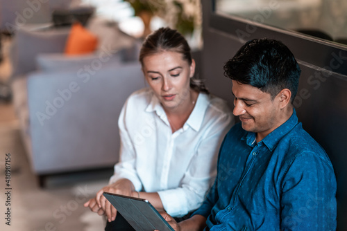 Multiethnic business people man with a female colleague working together on tablet computer in relaxation area of modern startup office