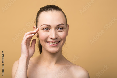 Happy caucasian girl with beautiful face touching healthy facial skin isolated on beige studio background. Skin care concept.